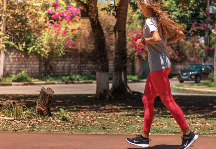 A woman jogs on a path surrounded by trees and vibrant flowers, embodying a healthy lifestyle.