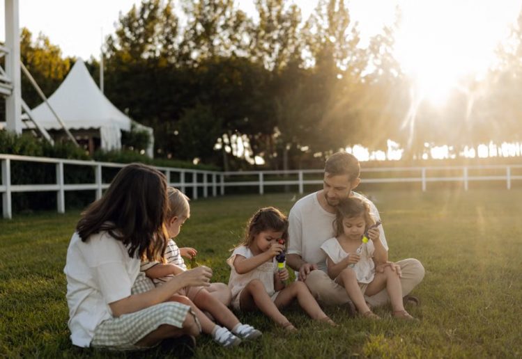 Family sitting on grass enjoying leisure time outdoors, with sun setting in the background.