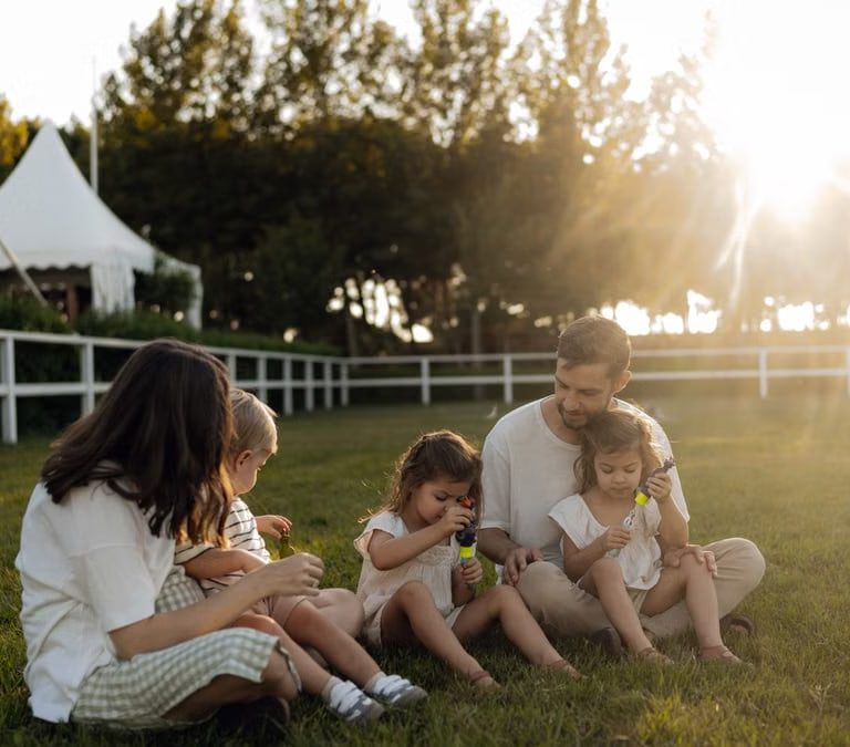 Family sitting on grass enjoying leisure time outdoors, with sun setting in the background.